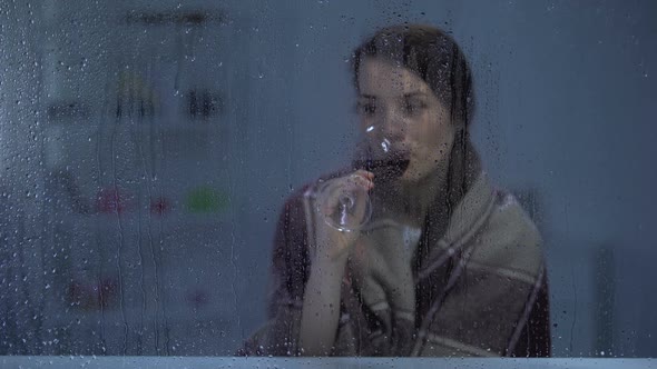 Pensive Woman in Blanket Drinking Wine Behind Rainy Window Cold Evening alt