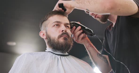 View From the Bottom of Face of Young Bearded Man Who is Sitting on the Barber's Chair Facing the alt