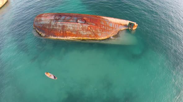 Aerial shot of young woman sup standup paddleboarding near a shipwreck in the Caribbean. alt