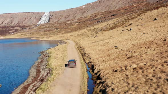 Car On Dirt Track By Fjord Towards Waterfall On Mountain alt