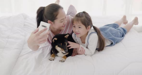 Mother and daughter playing with black dog on bed (try to taking a photo)