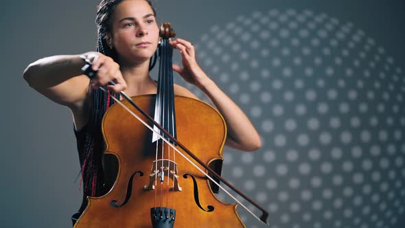 Young Beautiful Woman Playing on Cello in the Spotlight. Grey Background