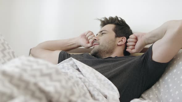 Sleepy Man Yawning on Bed in Morning. Handsome Guy Stretching in Bedroom. alt