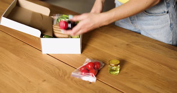 Woman open a delivery box meal kit and pulls fresh ingredients alt