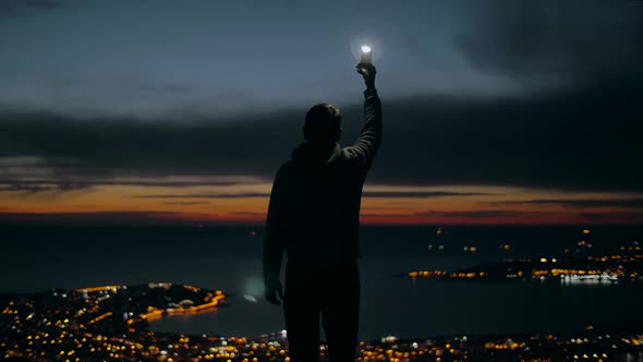 Man raises a glowing torch against a panorama of a night city