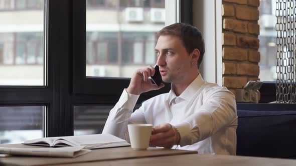 Businessman Talking on the Phone in a Cafe and Drinking Coffee alt