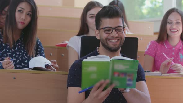 Smiling Indian Young Guy Reading Book at Lecture Hall alt