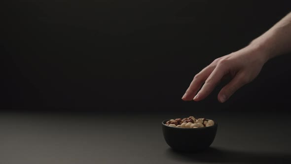 Slow Motion Man Take Roasted Hazelnuts From Black Bowl on Black Paper Background alt