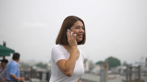 A beautiful Asian woman talks to a cell phone beside the river.