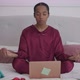Young African American Yogi Woman in Pajamas Meditating Sitting on Bed with Laptop