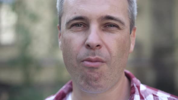 Headshot of Confident Caucasian Greyhaired Man Smoking Outdoors Blowing Smoke Looking at Camera alt