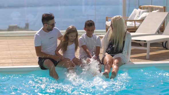 Funny Family of Four Sitting Near the Pool on the Background of the Sea Enjoying a Vacation