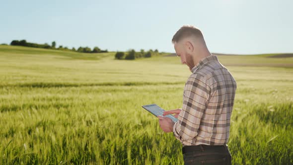 The Farmer is Standing Near the Field and Working with a Tablet alt