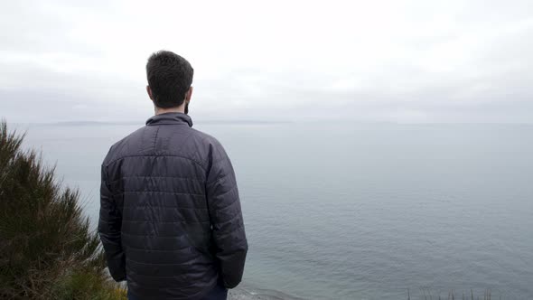 Man stoically gazes out into the Pacific Ocean. alt