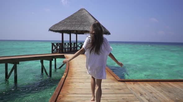Lady in white dress runs on a pier near water bungalows in the Maldives. Travel time. Honeymoon.