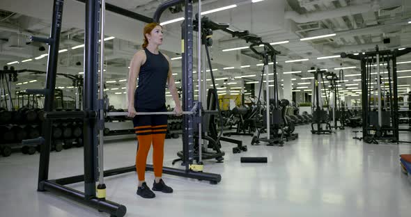 Woman in Tracksuit Has Training with Barbell in Spacious Gym alt