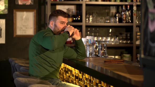 A Man with a Beard Drinks Alcohol and Talks on the Phone