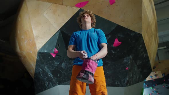 Portrait of a Man Climber Guy Stands Against the Background of a Climbing Wall and Use Magnesia alt