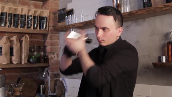 Handsome barista shakes a shaker in cafe.