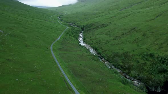 Pan up drone shot reveals country road in Scottish Highlands alt