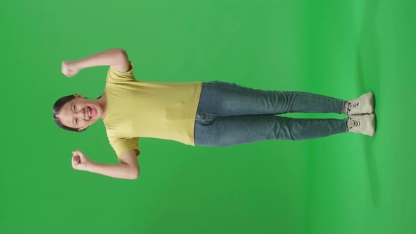 Full Body Of Cheerful Young Asian Kid Girl Celebrating While Standing On Green Screen In The Studio alt
