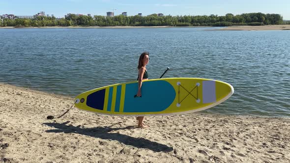 Caucasian Woman Walks Along the Beach and Carries a Sup Board on the River in the City alt