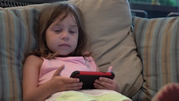 The child sits in a chair and looks into the smartphone or cell phone. 