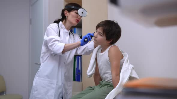 Caucasian Boy Sitting on Examination Couch As Smiling Doctor Checking Ears with Otoscope alt