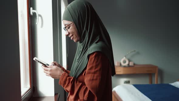 Positive Muslim woman wearing eyeglasses leafing tape by phone and looking at the camera alt