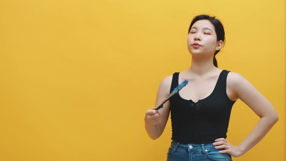 Annoyed Overheated Asian Woman Waving Fan. Isolated on Yellow Background alt