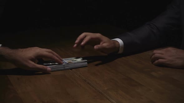Businessman giving money to his partner on the table in the dark