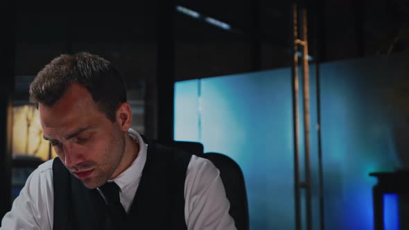 A Man Sits at a Table in the Office Works with a Computer and Documents alt