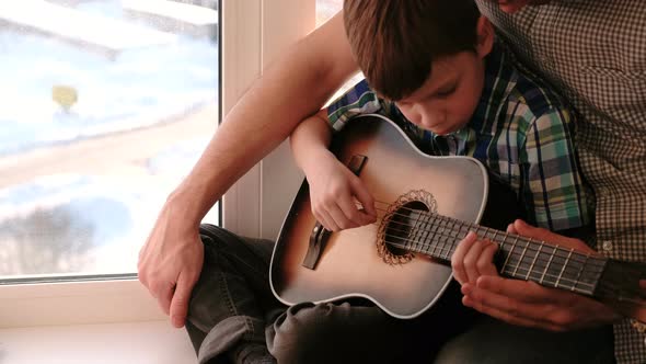 Dad Teaches His Son To Play the Guitar, Sitting on the Windowsill