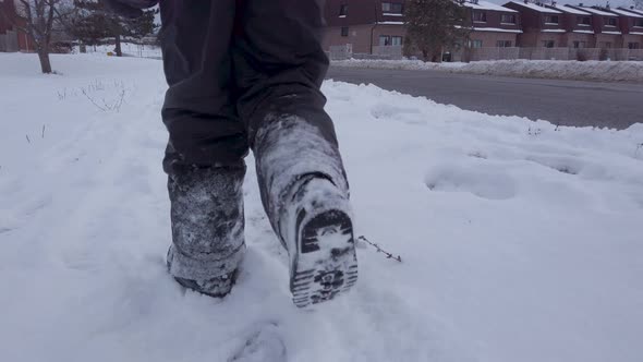 Young child walking in snow alongside road wearing grey snowpants boots gloves in winter alt