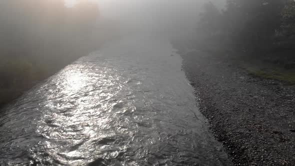 River Flowing Through Mountain Village in a Foggy Morning alt