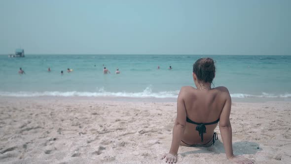 Lady Looks at Endless Blue Ocean with People Backside View alt