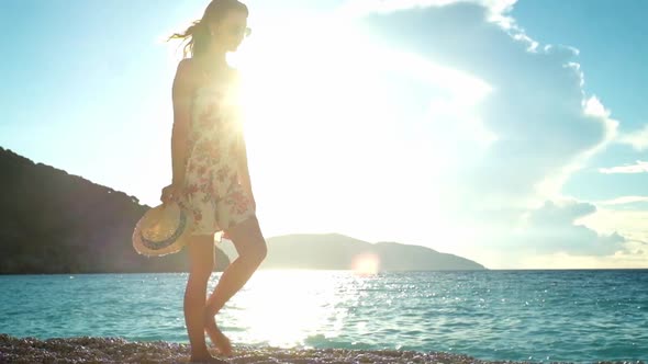 Young woman in dress walking on a beach at sunset