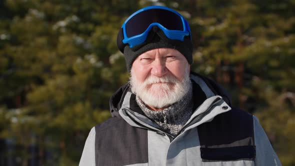 Elderly Attractive Man in Ski Goggles Leads an Active Lifestyle Stands Background of Forest Trees in