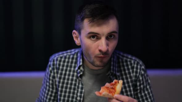 Portrait of Young Hipster Man Eating Pizza Watching Favorite Film on TV While Relaxing at Sofa