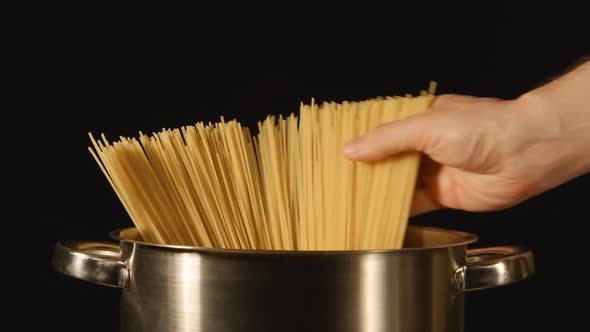 A cook puts down a bunch of spaghetti in a steel pot
