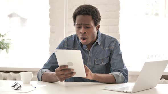 Stressed African Man Reacting to Loss on Tablet alt