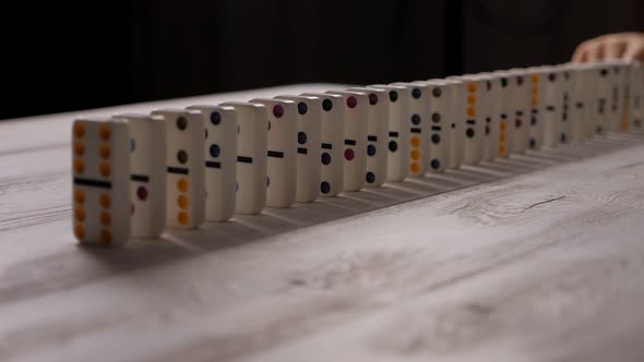 White Dominoes with Multicolored Dots Slowly Fall on a Light Wooden Background alt