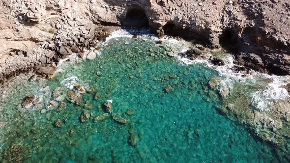 Aerial View of a Cave with Crystal Clear Waves at a Rocky Coast with Clear Blue Water