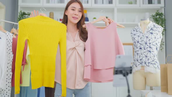 Asian beautiful woman sell cloth product online live streaming at home. alt
