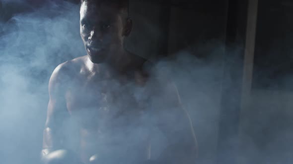 African american man wearing boxing gloves banging fists together in dark smoky room alt