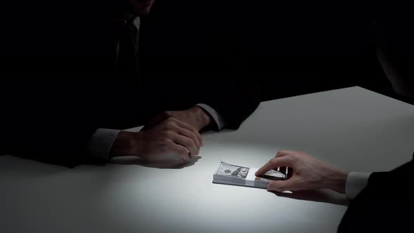 Businessman giving bribe money to his partner on the table in dark room