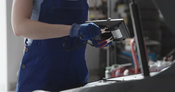 Professional female mechanic doing a car service, she is testing the battery with a tester