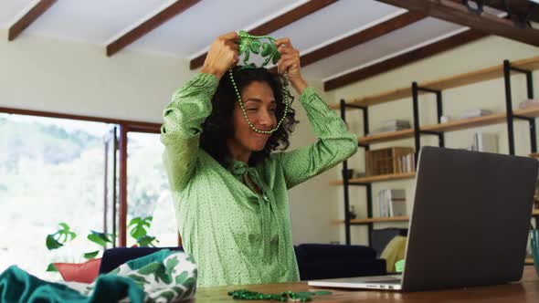 Mixed race woman in green beads necklace and costume having a video call on laptop at home alt