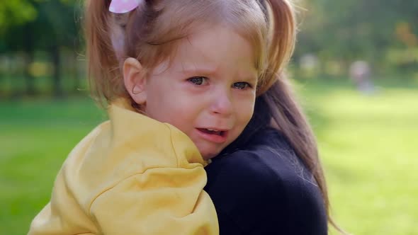 Close-up portrait of a little charming girl crying in her mother arms