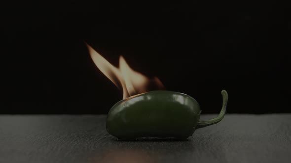 Green jalapeño chili pepper on fire on black background
